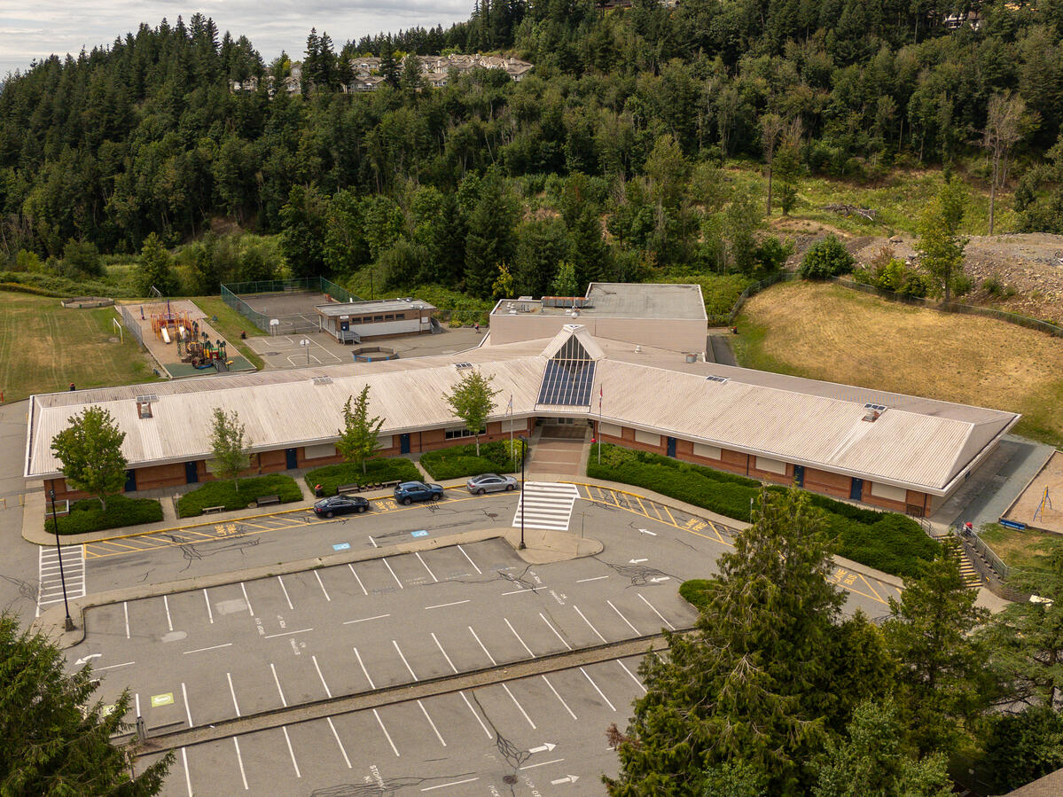 Exterior image of elementary school entrance. Playground shown behind the school, along with many trees and a homes in a neighbourhood.